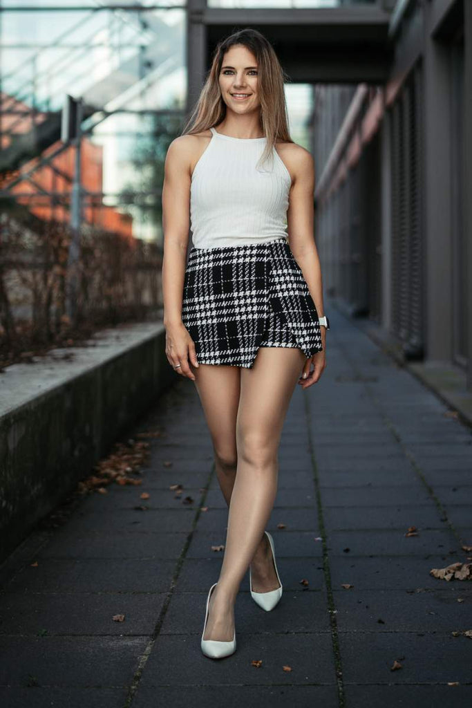 Girl wearing glossy pantyhose with white tank top, plaid skirt, and white stilettos 