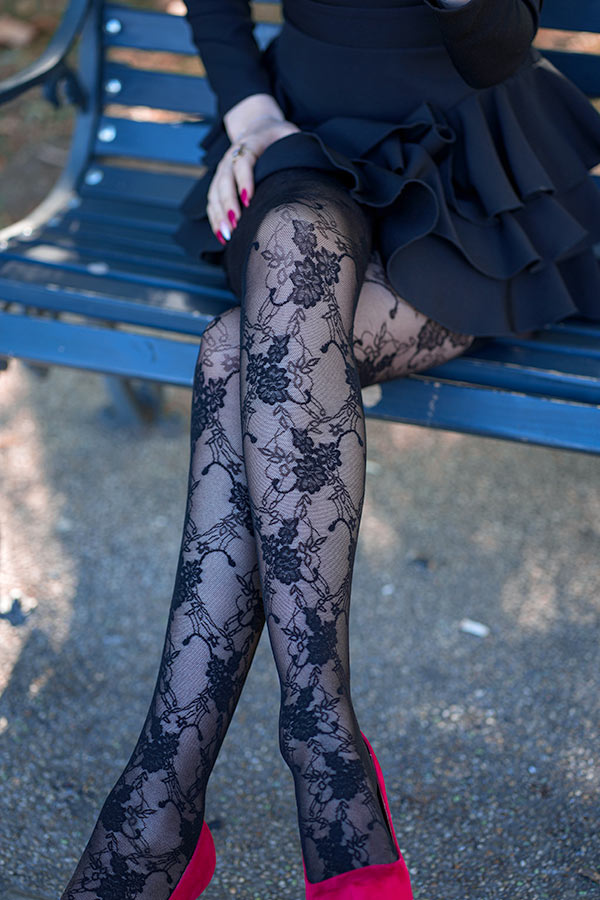 Girl sitting on bench wearing black dress, lace stockings, and red velvet heels